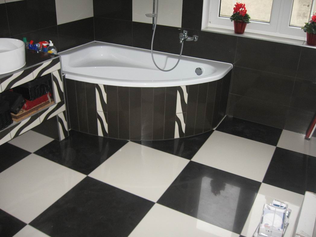 Czarno-biała łazienka z narożną wanną obudowaną płytkami imitującymi zebrę, podłoga w szachownicę, umywalka nablatowa na szafce w tym samym wzorze, okno z czerwonymi kwiatami.